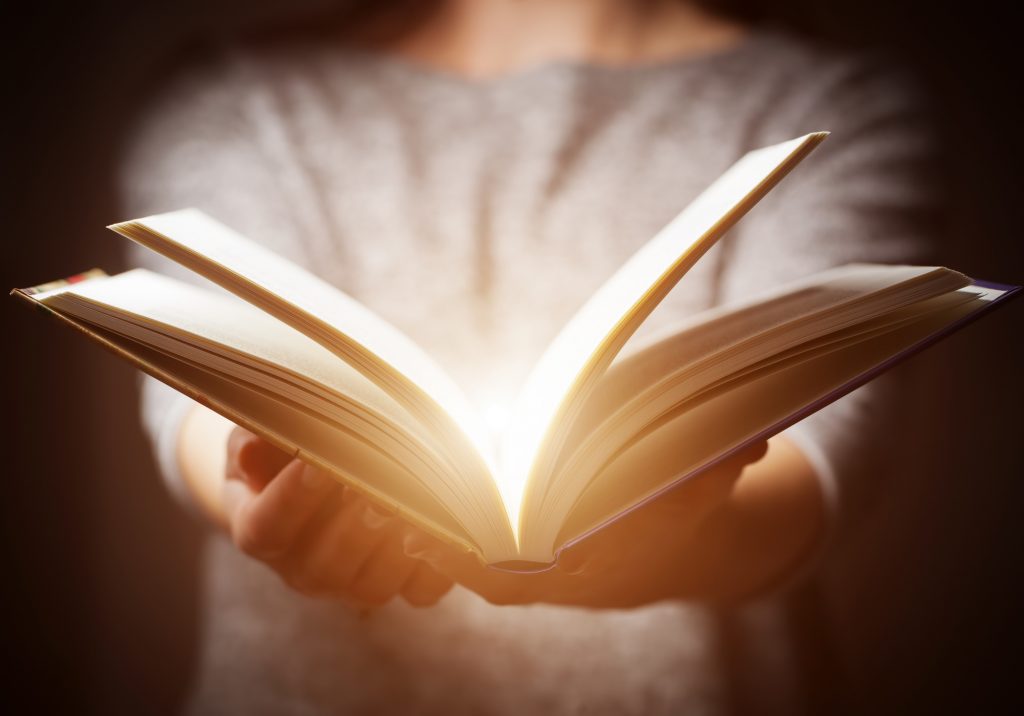 Hands holding open glowing book