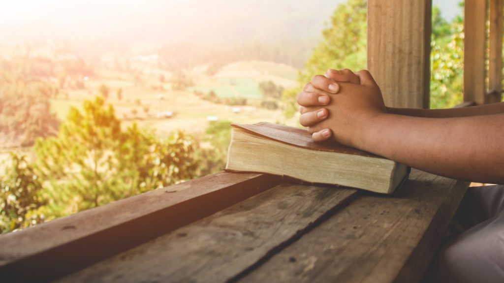 Hands praying on Bible overlooking valley