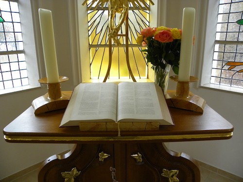 Open Bible on table with candles, flowers, and stained glass window in background